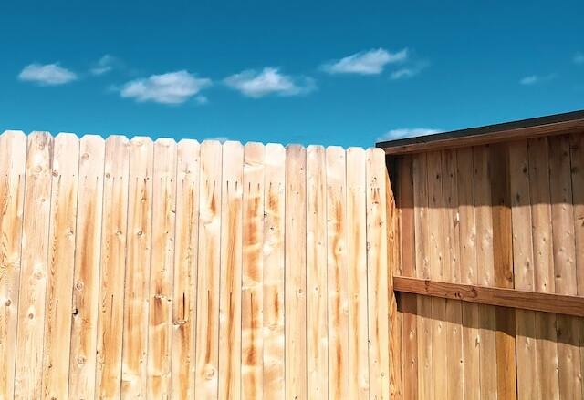 the corner of a wood fence with a blue sky and a few clouds above