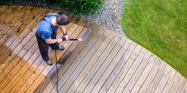man cleaning terrace with a power washer - high water pressure cleaner on wooden terrace surface